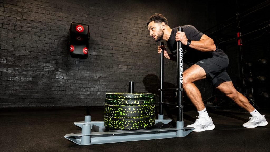 Athlete demonstrating proper body mechanics during a heavy sled push workout with a forward lean, neutral spine, engaged core, and powerful leg drive on a gym turf track.